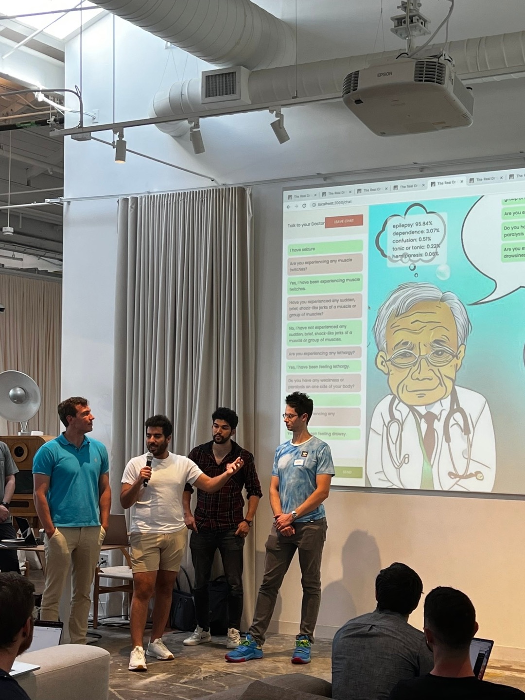 The four of us presenting Dr Claude to the judges and audience at Shack15. Behind us, the demo is projected: a chat transcript of the doctor's questions and the patient's answers on the left, a cartoon doctor on the right, and a thought bubble showing the live differential with epilepsy at 95.84%.